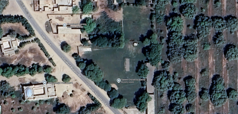 Aerial view of Tareen Cricket Academy in Lodhran, Pakistan, showcasing lush green pitches and training facilities surrounded by rural fields, with young players practicing under the guidance of coaches.