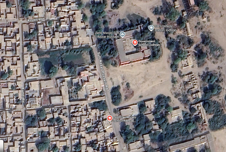 Exterior view of Government Elementary School (GES) Lodhran City, Punjab, Pakistan, showing a modest brick building with a courtyard where students gather, surrounded by green fields near the Sutlej River. Middel Schools